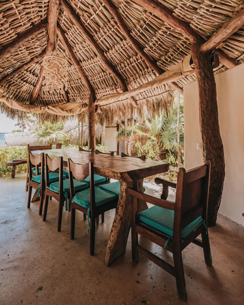 Thatch-roofed outdoor dining table with green-cushioned chairs at Casa Viento, Papaya Playa Project