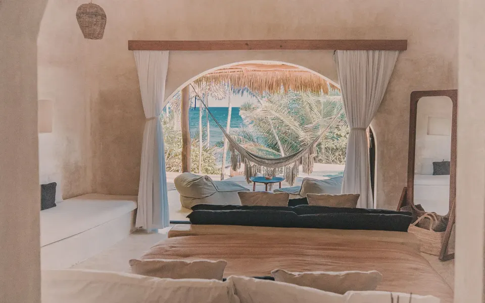 Ocean-view casita interior framed by arch with hammock and sea beyond at Papaya Playa Project