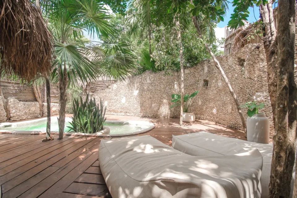 Wooden deck lounge area looking toward a private pool and stone wall at Papaya Playa Project
