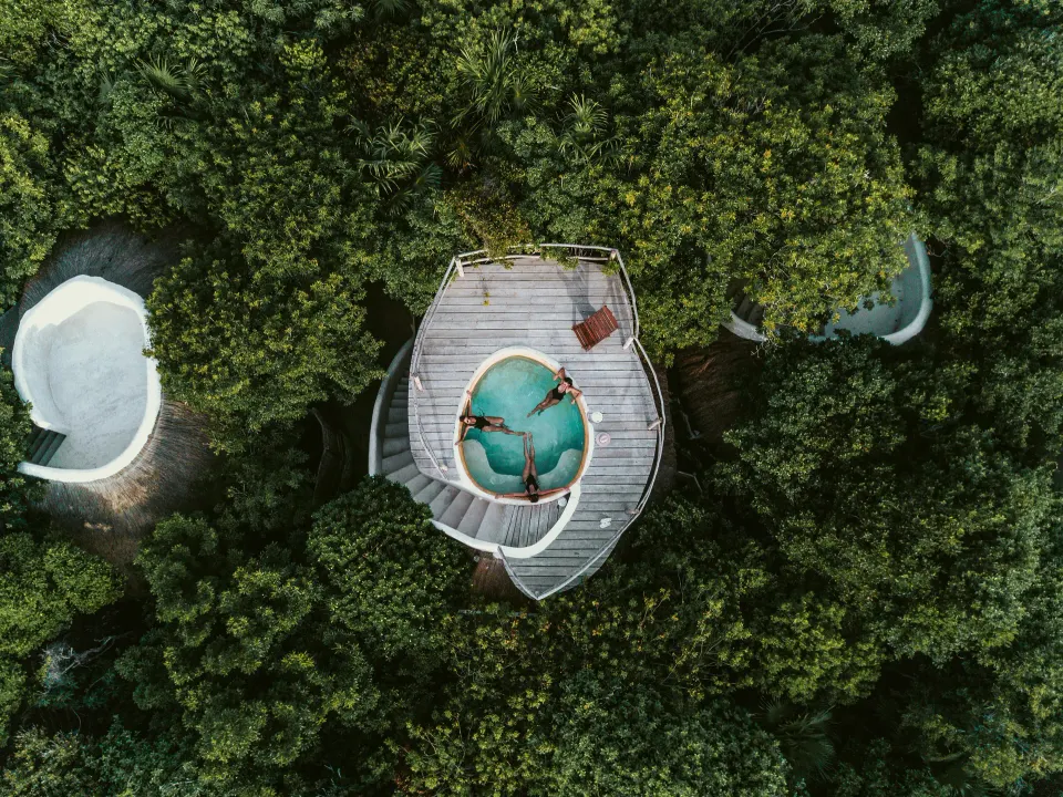 Aerial view of a rooftop casita pool with two people floating, surrounded by jungle at Papaya Playa Project