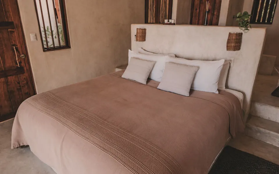 King bed with neutral linen and rustic wood doors in a casita at Papaya Playa Project