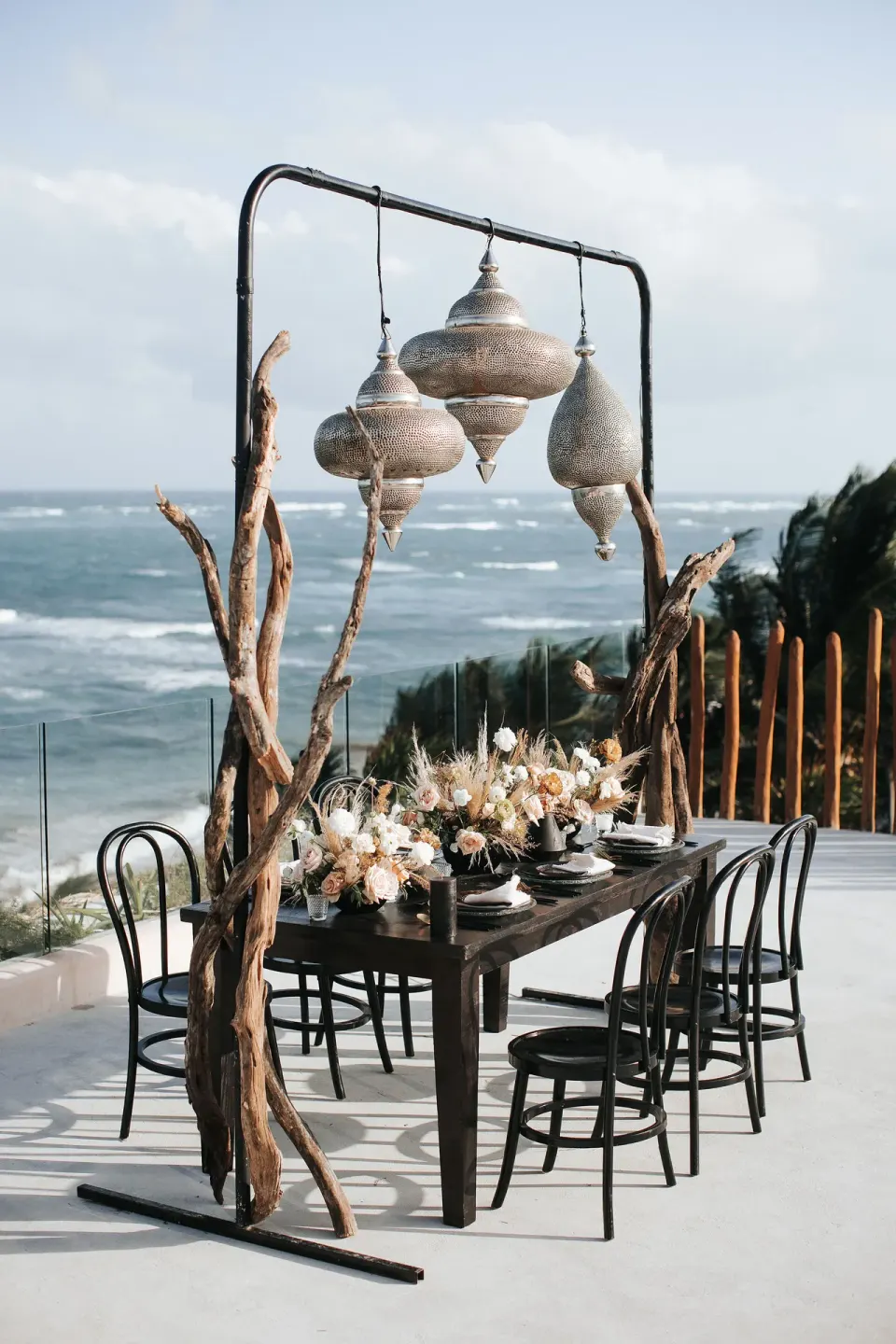Close view of an ocean-facing table with sculptural lamps and driftwood at Papaya Playa Project.