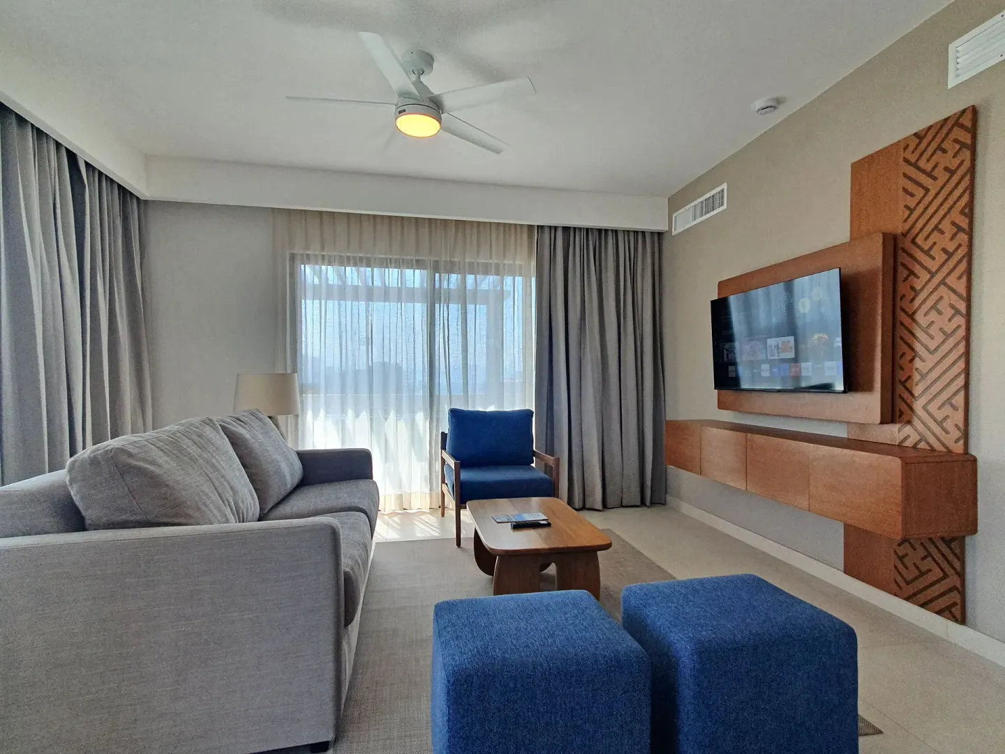 Contemporary living area with sofa, blue ottomans, chair, and TV at Paradise Village Beach Resort and Spa.