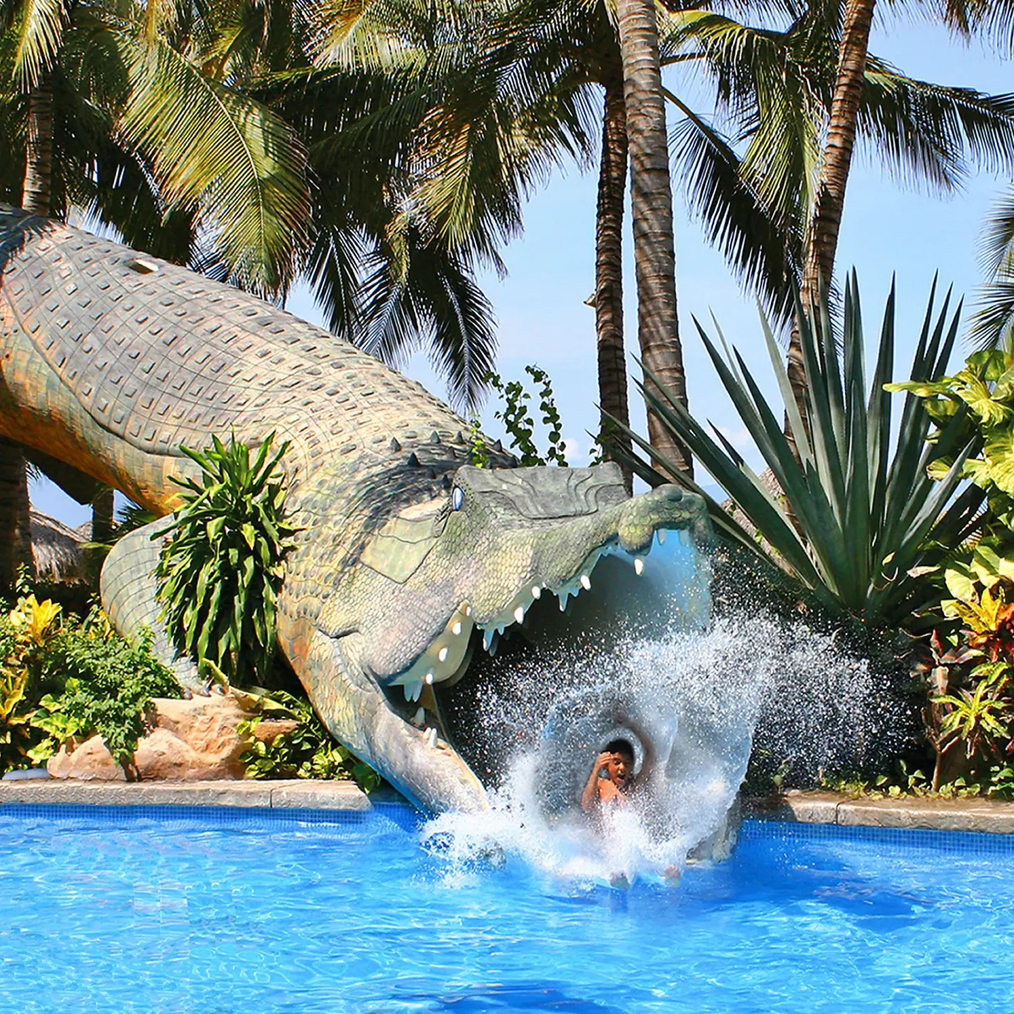 Crocodile-themed pool slide splashing into the water at Paradise Village Beach Resort and Spa.