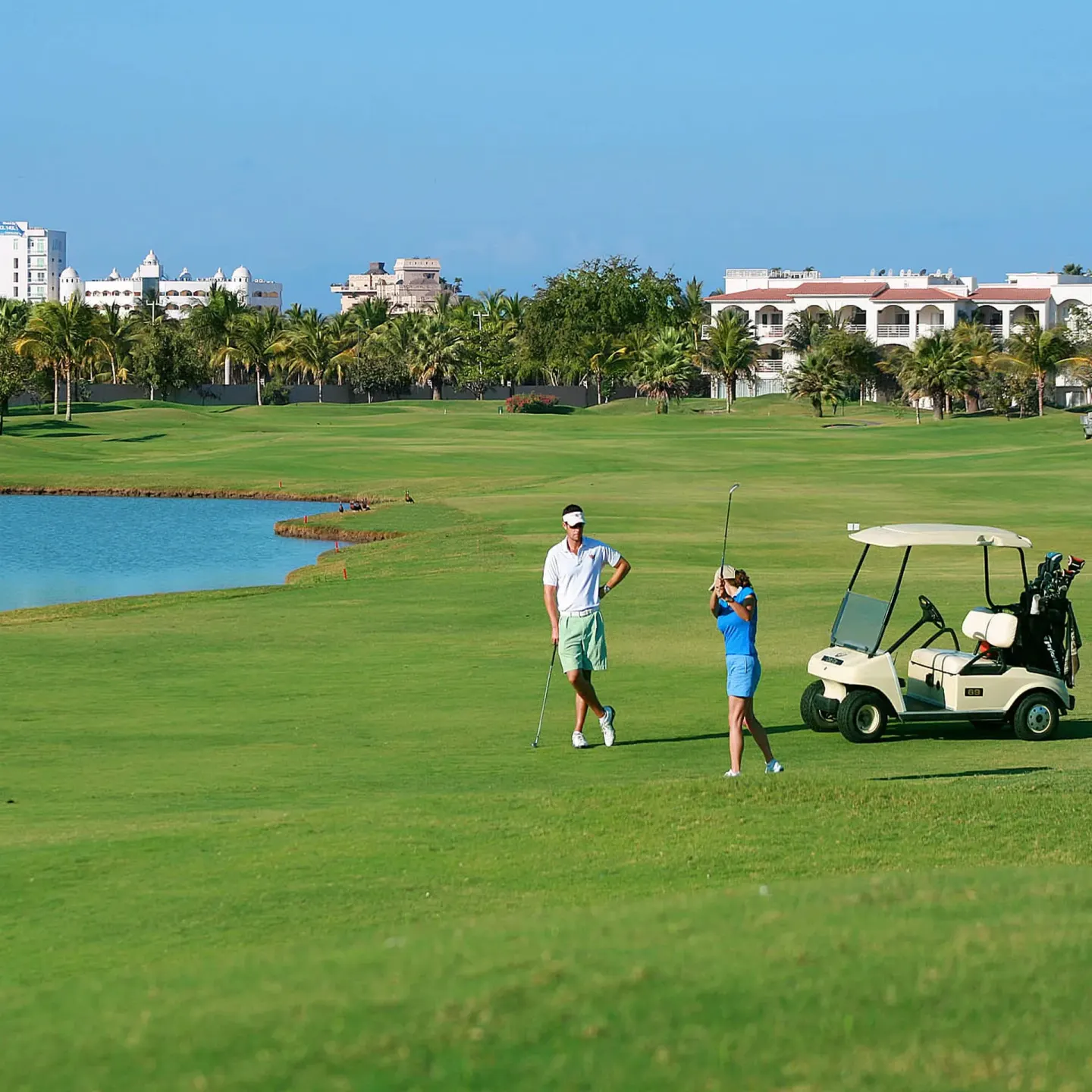 Golfers and a golf cart on a green course near Paradise Village Beach Resort and Spa.