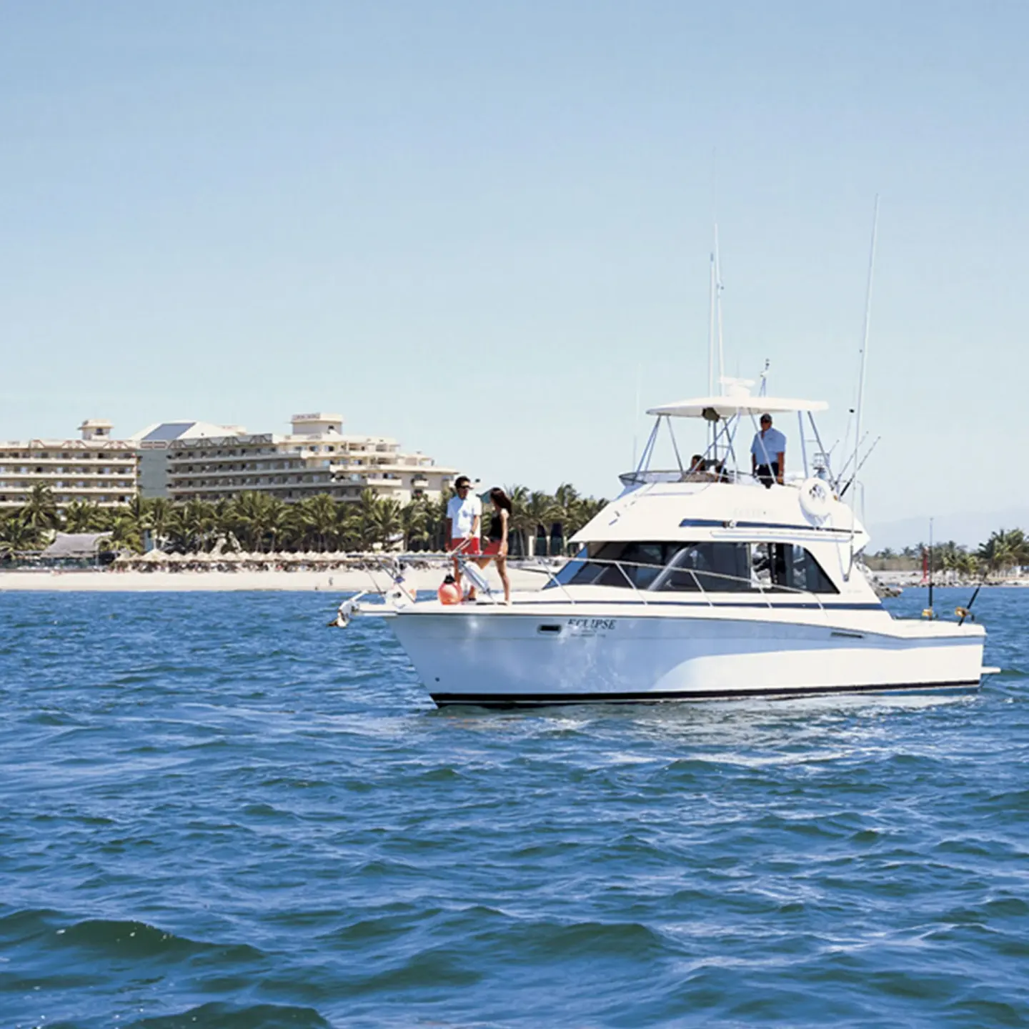 White motor yacht on the water off Paradise Village Beach Resort and Spa with the resort shoreline behind.