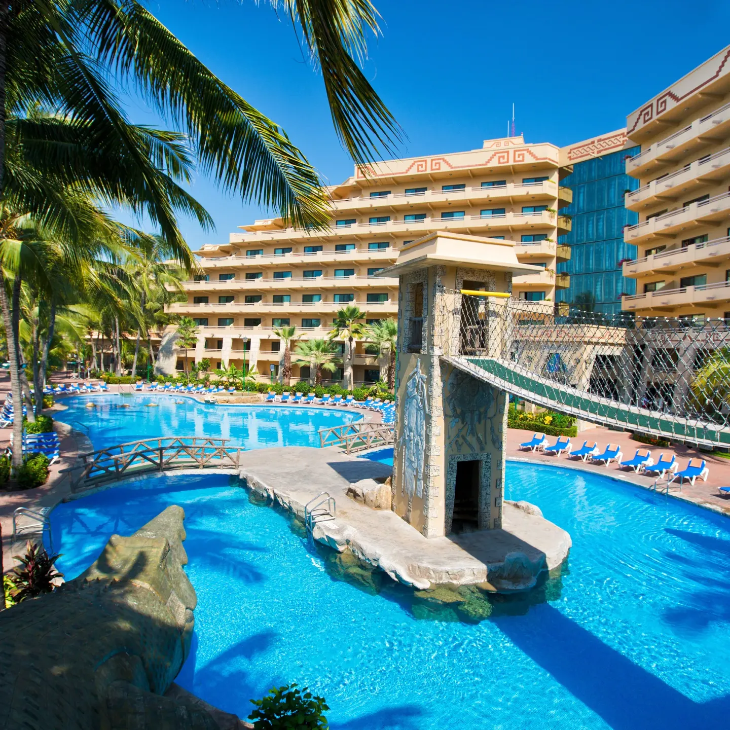 Pool complex with a suspension bridge and hotel buildings at Paradise Village Beach Resort and Spa.