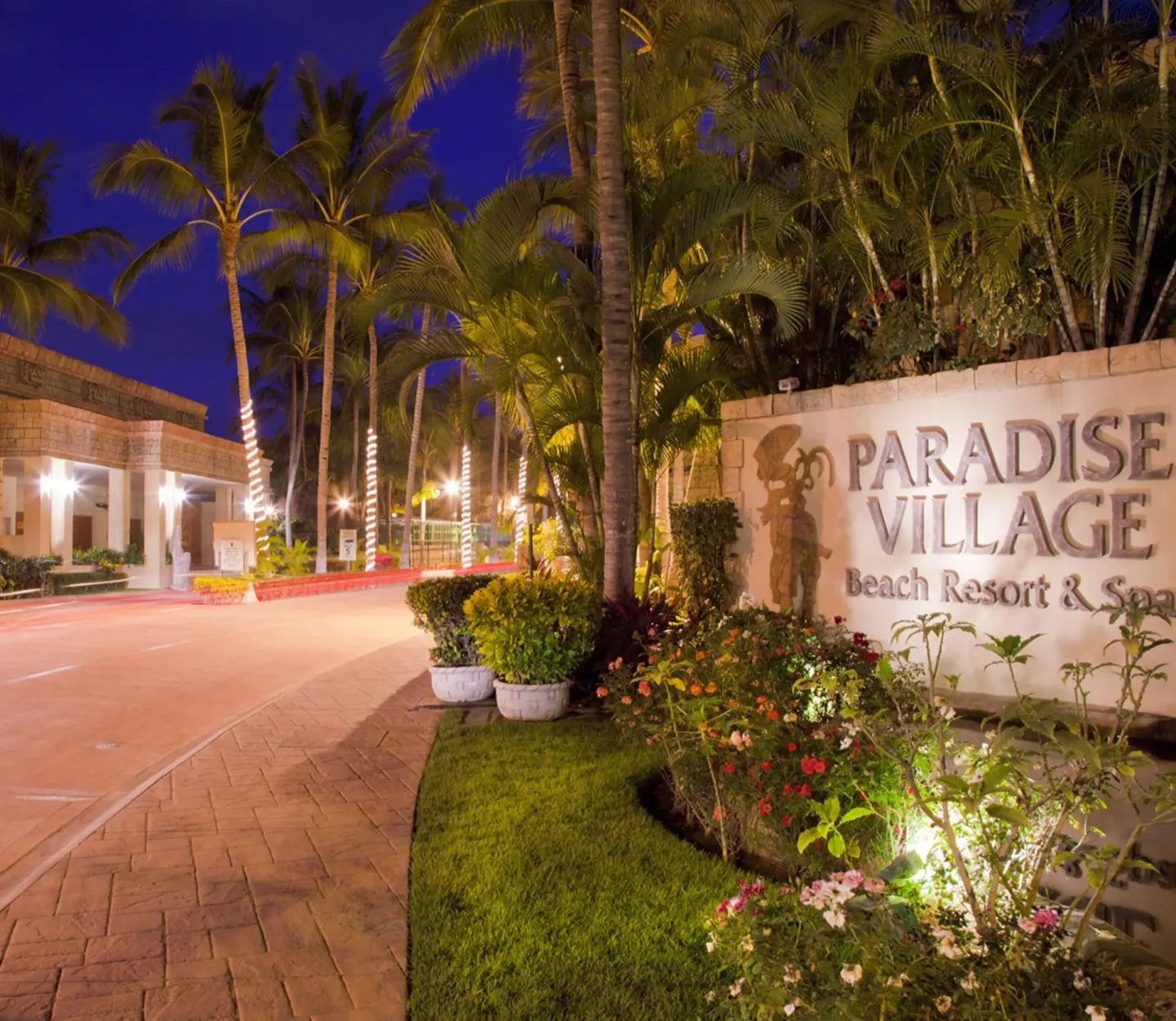Illuminated resort entrance sign and palm-lined drive at Paradise Village Beach Resort and Spa.