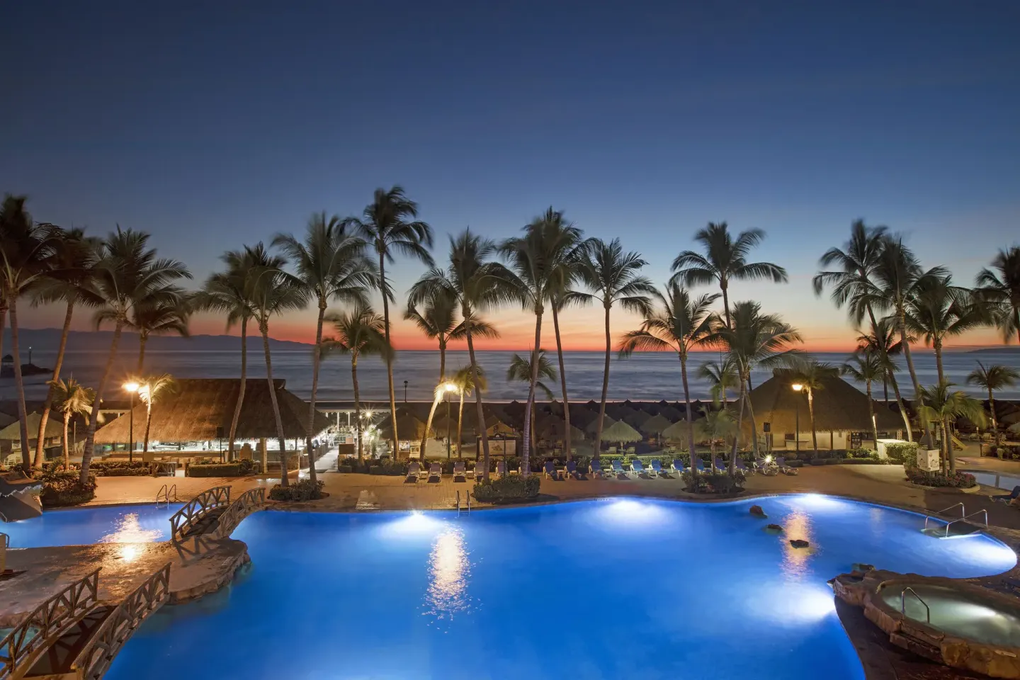 Illuminated resort pool, palm trees, and ocean at sunset at Paradise Village Beach Resort and Spa.