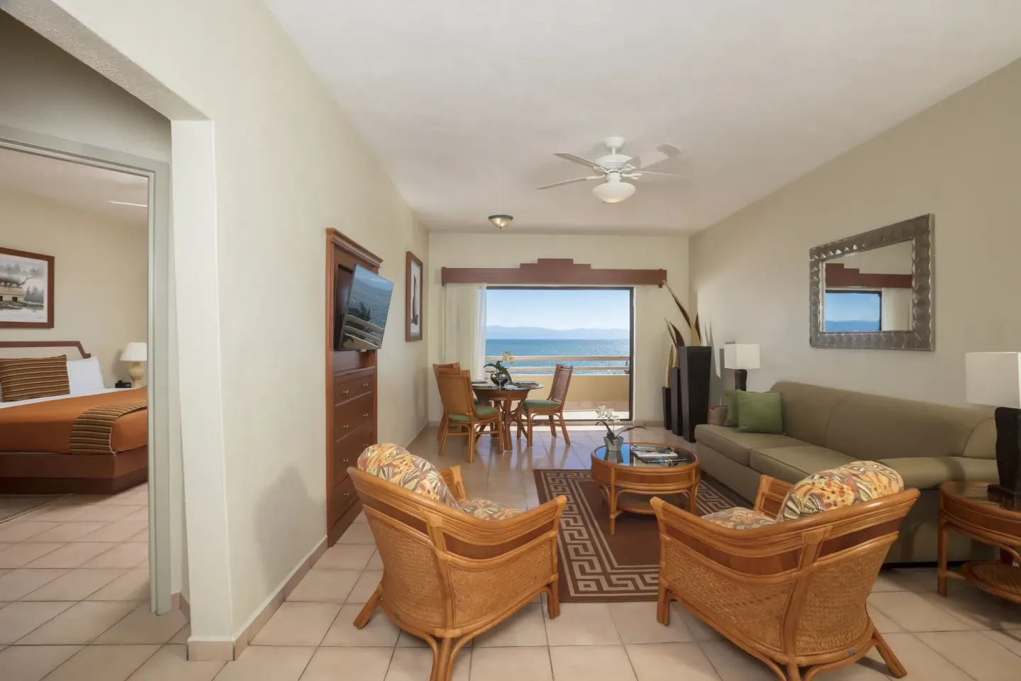Suite living room with sofa, wicker chairs, dining table, and ocean view at Paradise Village Beach Resort and Spa.