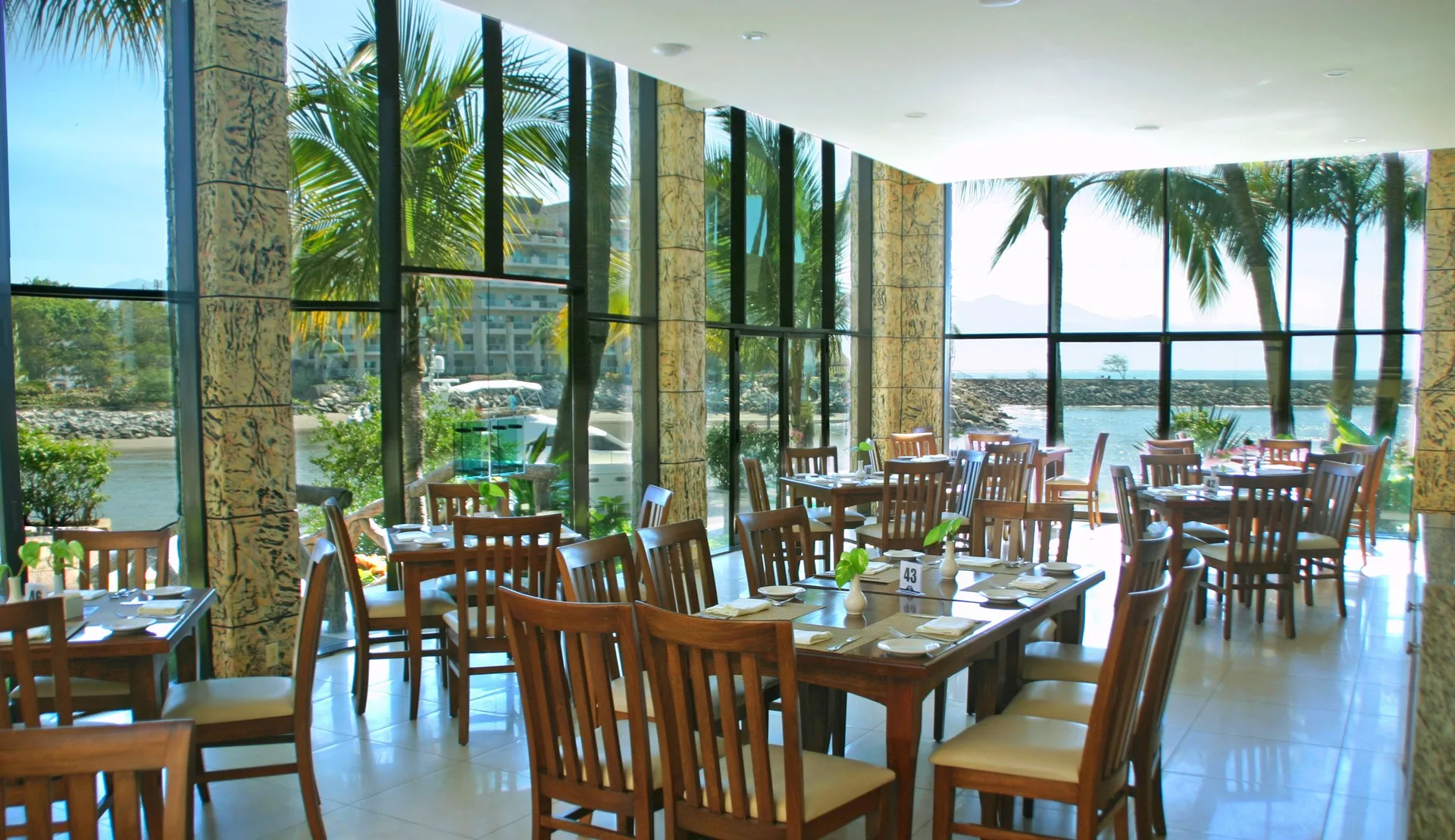 Waterside dining room at Paradise Village Beach Resort and Spa with wooden tables and tall windows.