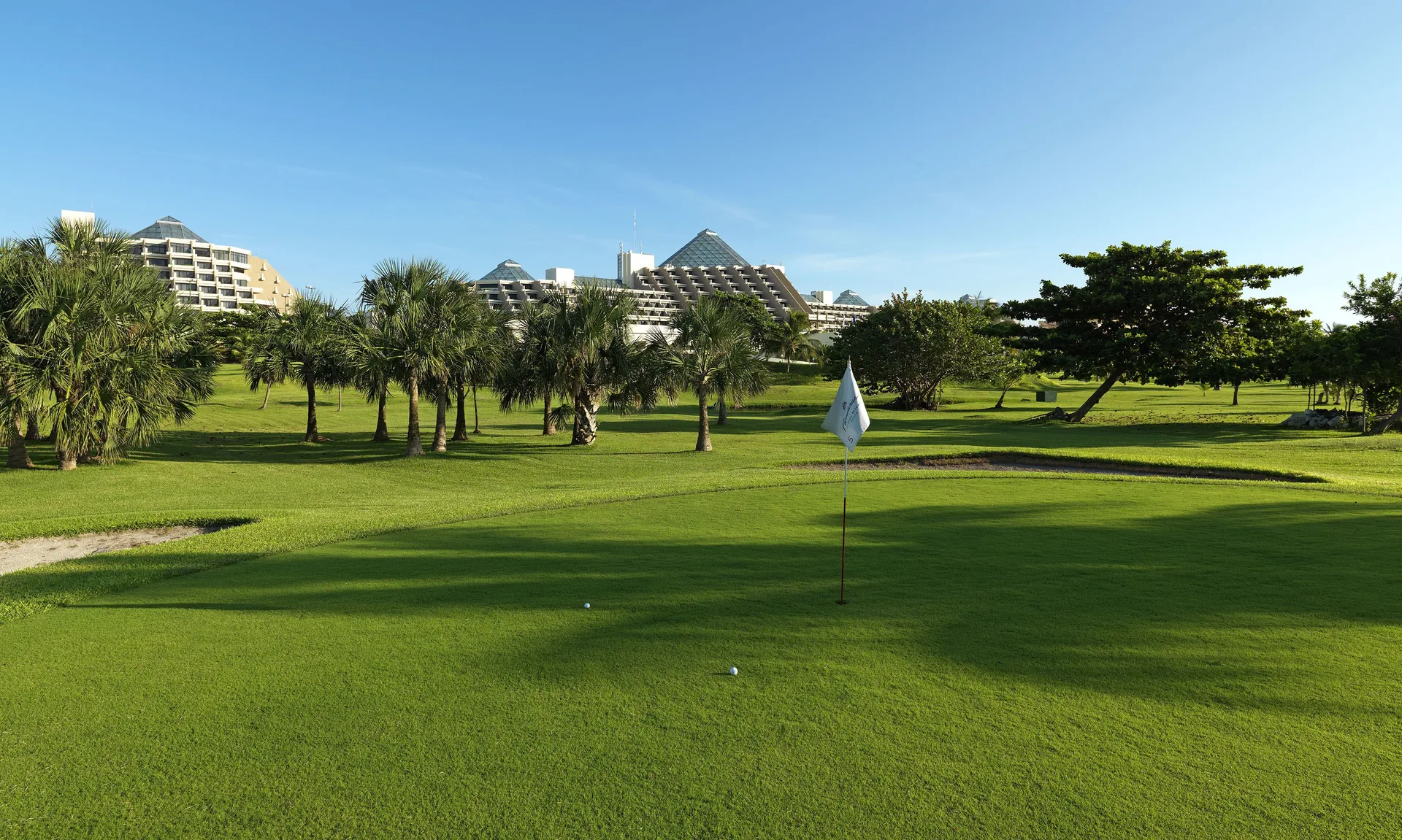 Golf green with palm trees and resort buildings in the distance at Paradisus Cancún.