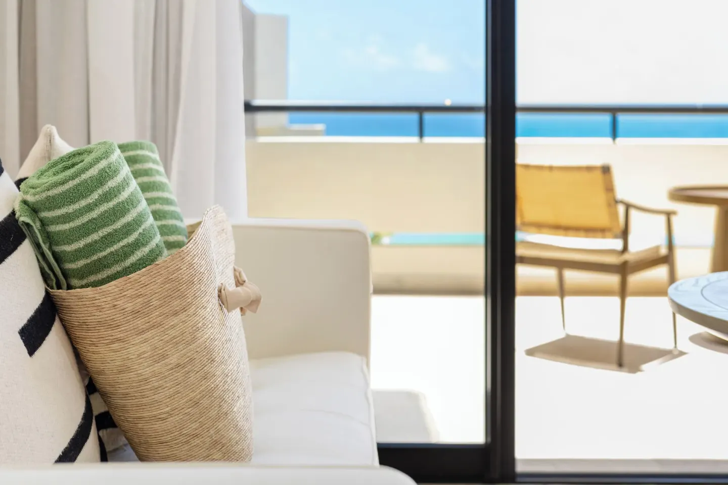 Guest room sofa with towel bag beside a sunny ocean-view balcony at Paradisus Cancún.