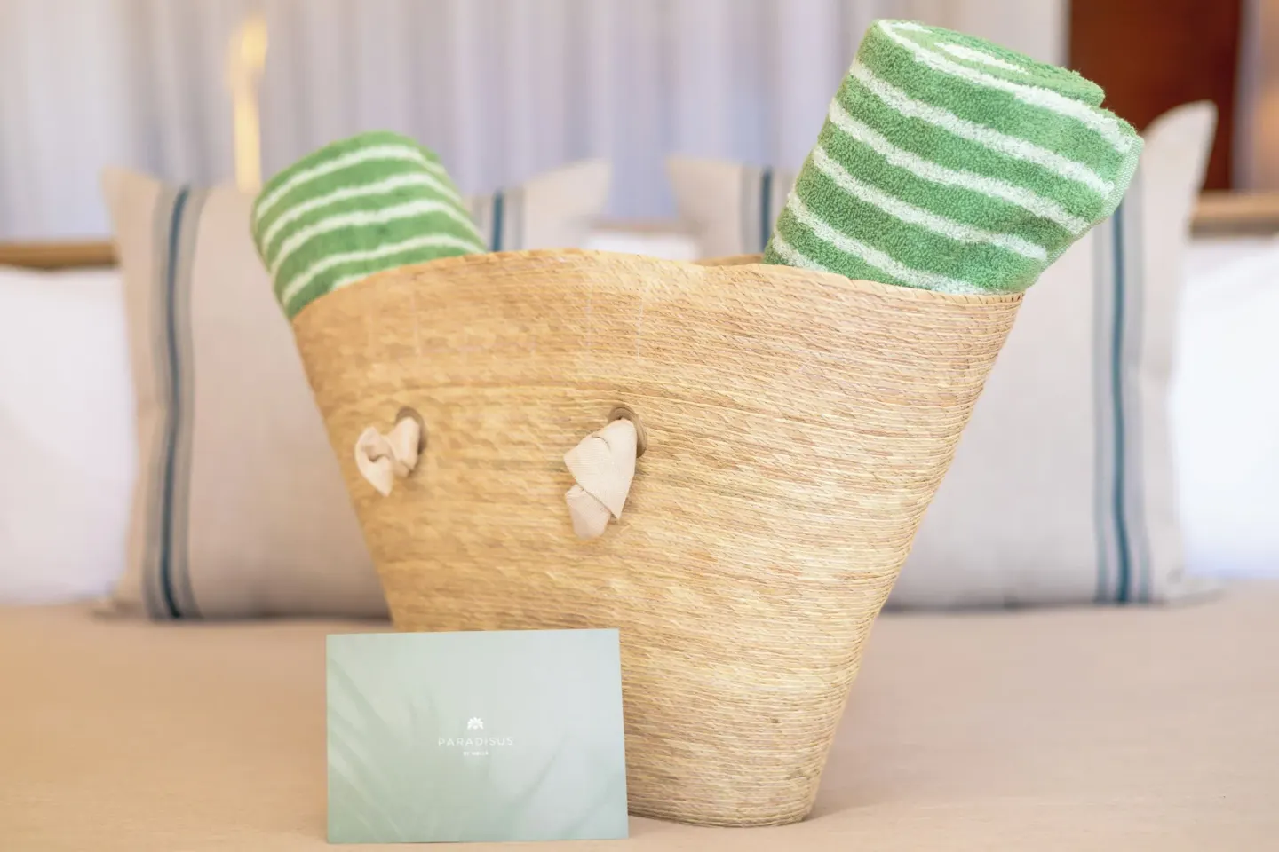 Woven beach bag with green striped towels on a guest room bed at Paradisus Cancún.