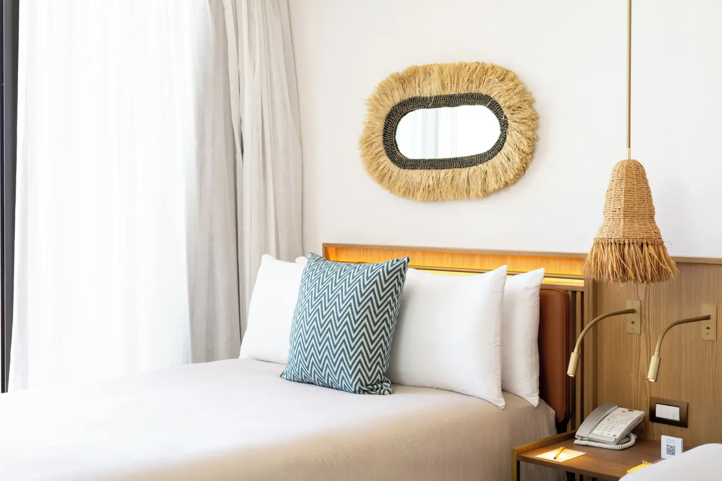 Close view of a guest room bed with woven wall mirror at Paradisus Cancún.