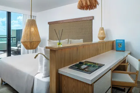 Guest room king bed and desk at Paradisus Cancún with woven lights and balcony doors.