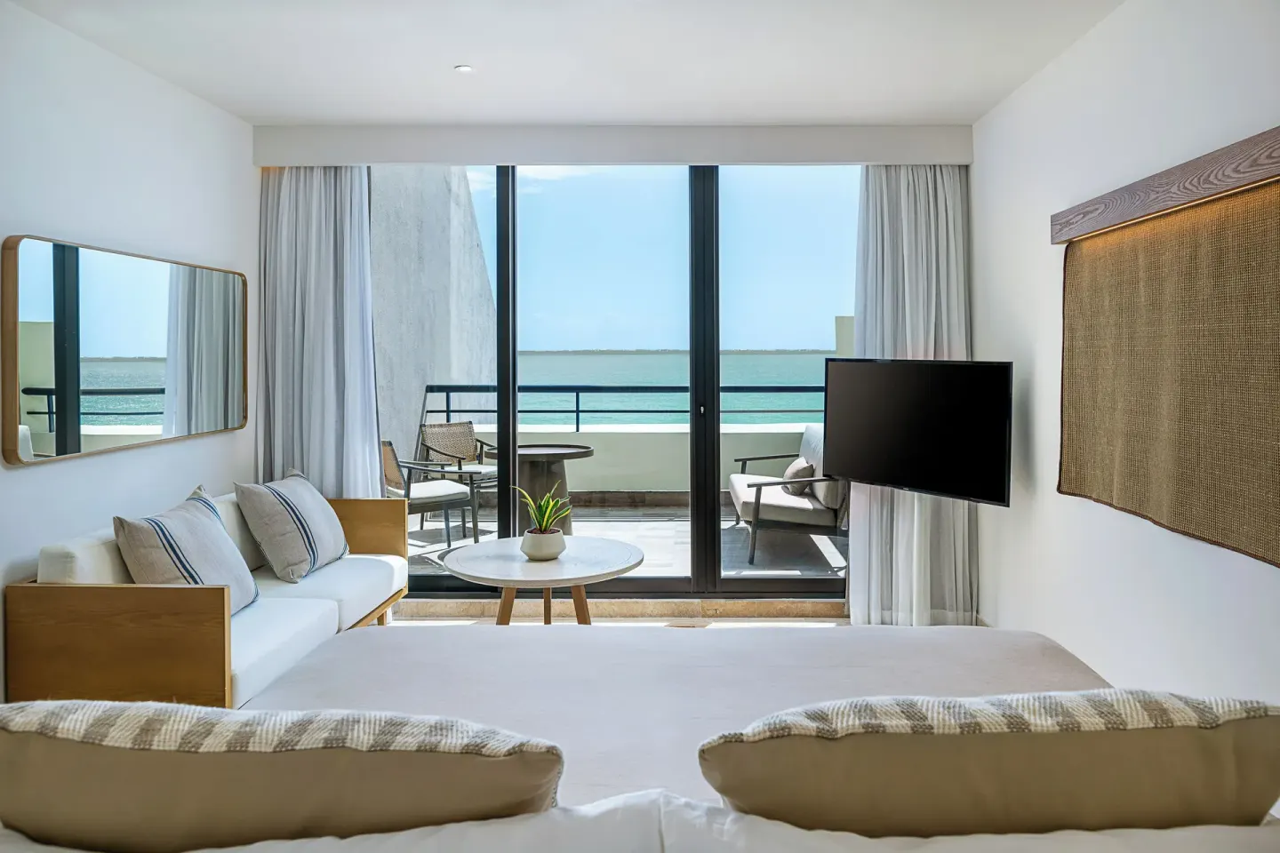 Guest room sitting area at Paradisus Cancún with a bed, sofa, TV, and balcony facing the ocean.