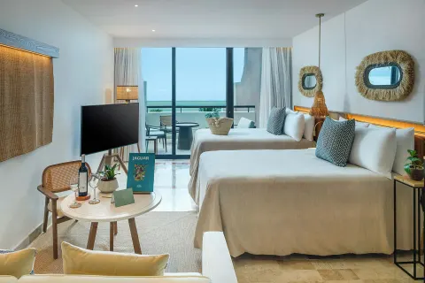 Guest room with two beds, TV, table setup, and balcony at Paradisus Cancún.