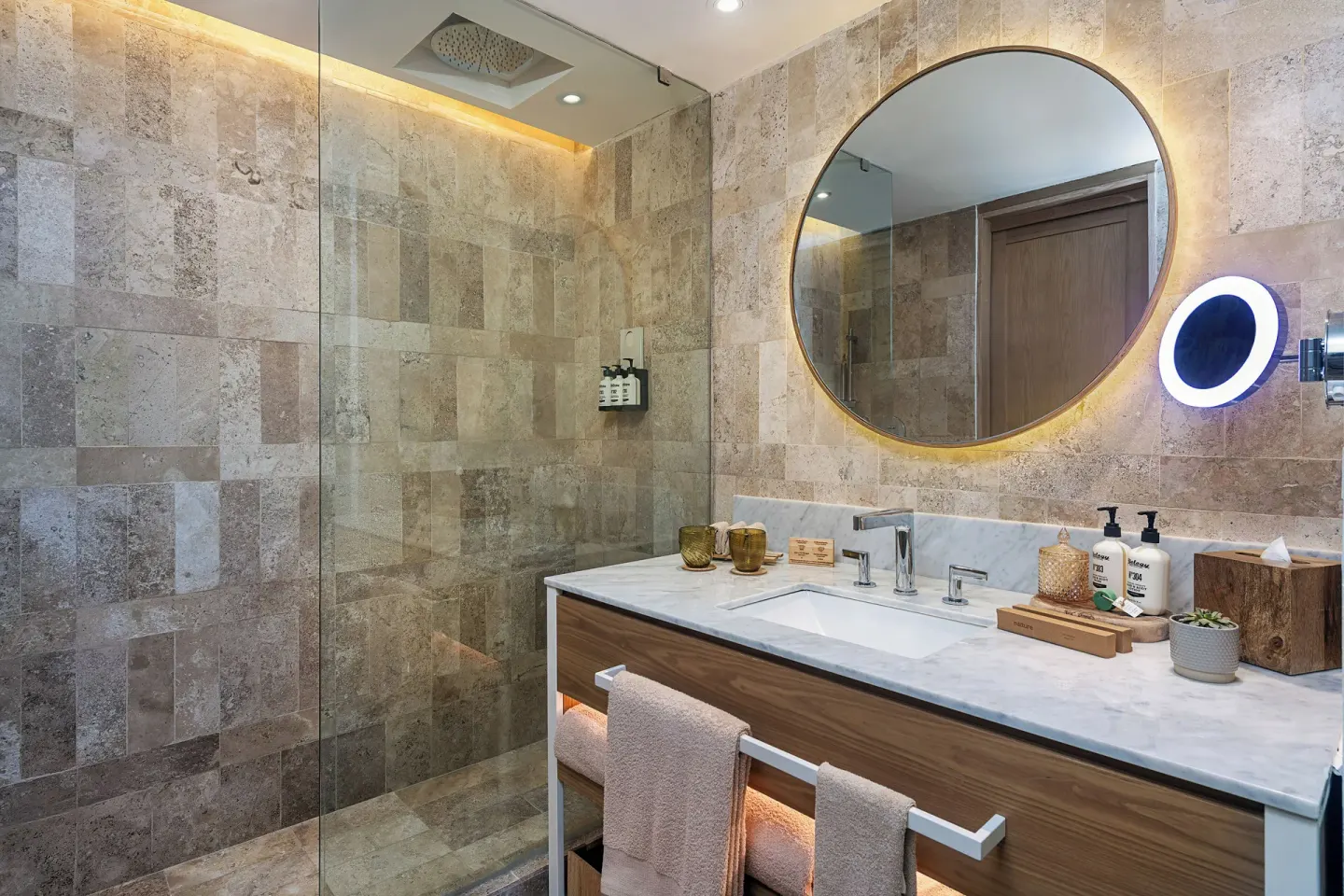 Stone bathroom with glass shower and backlit round mirror at Paradisus Cancún.