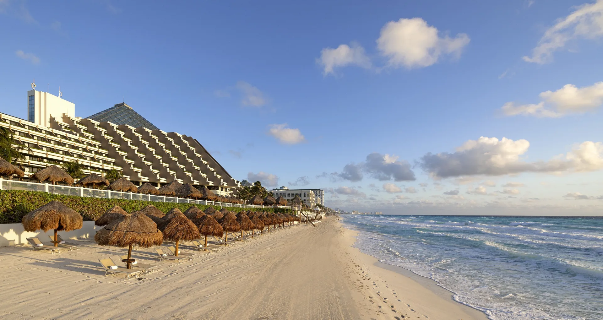 Wide beach with palapas, loungers and the resort building at Paradisus Cancún.