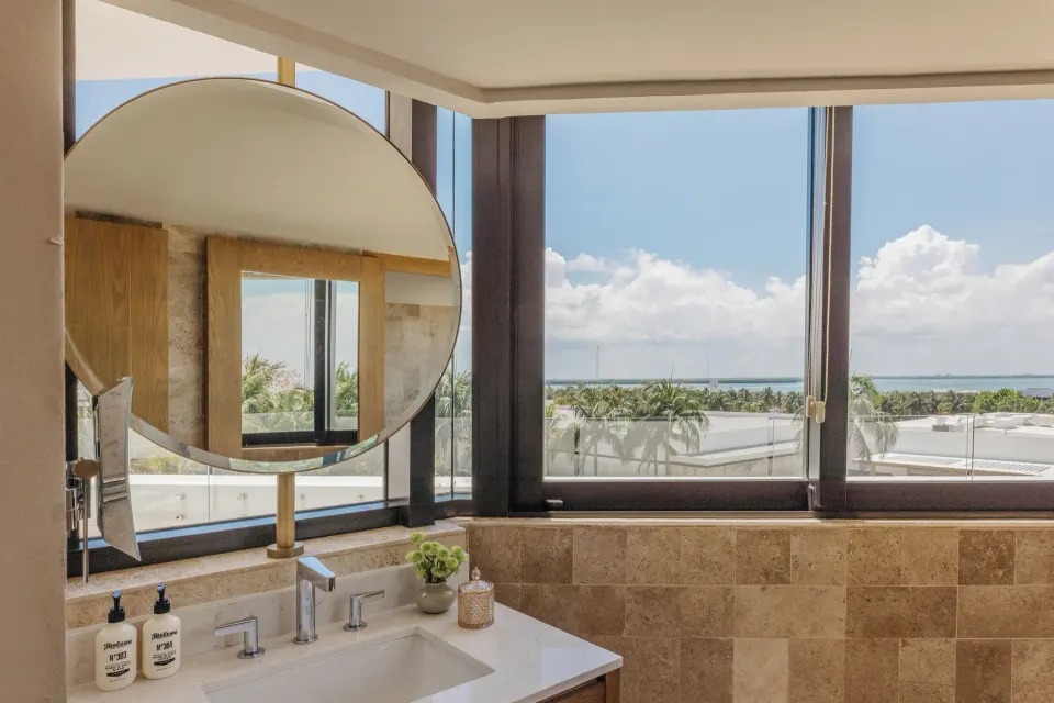 Bathroom vanity with round mirror and lagoon-facing windows at Paradisus Cancún.