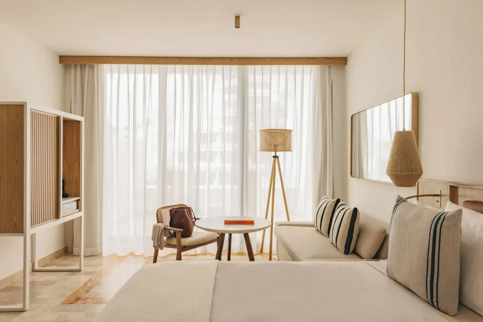 Junior Suite Ocean View sitting area and bed with sheer curtains at Paradisus Cancún.