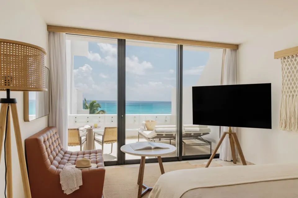 Ocean-view suite seating area, TV, bed and balcony lounge chairs at Paradisus Cancún.