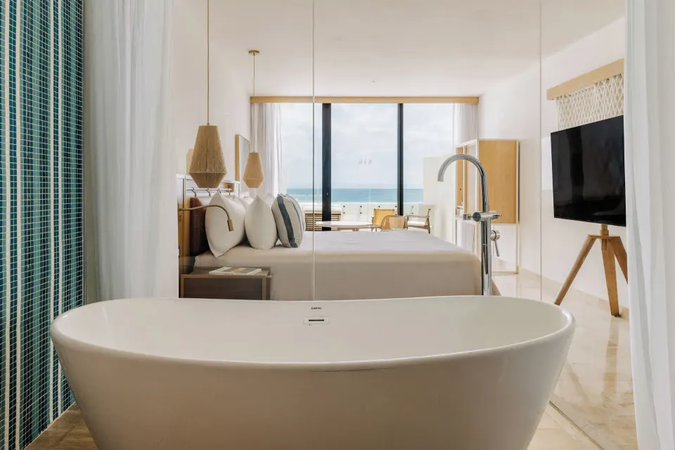 Suite bathtub facing the king bed, TV and ocean-view balcony at Paradisus Cancún.