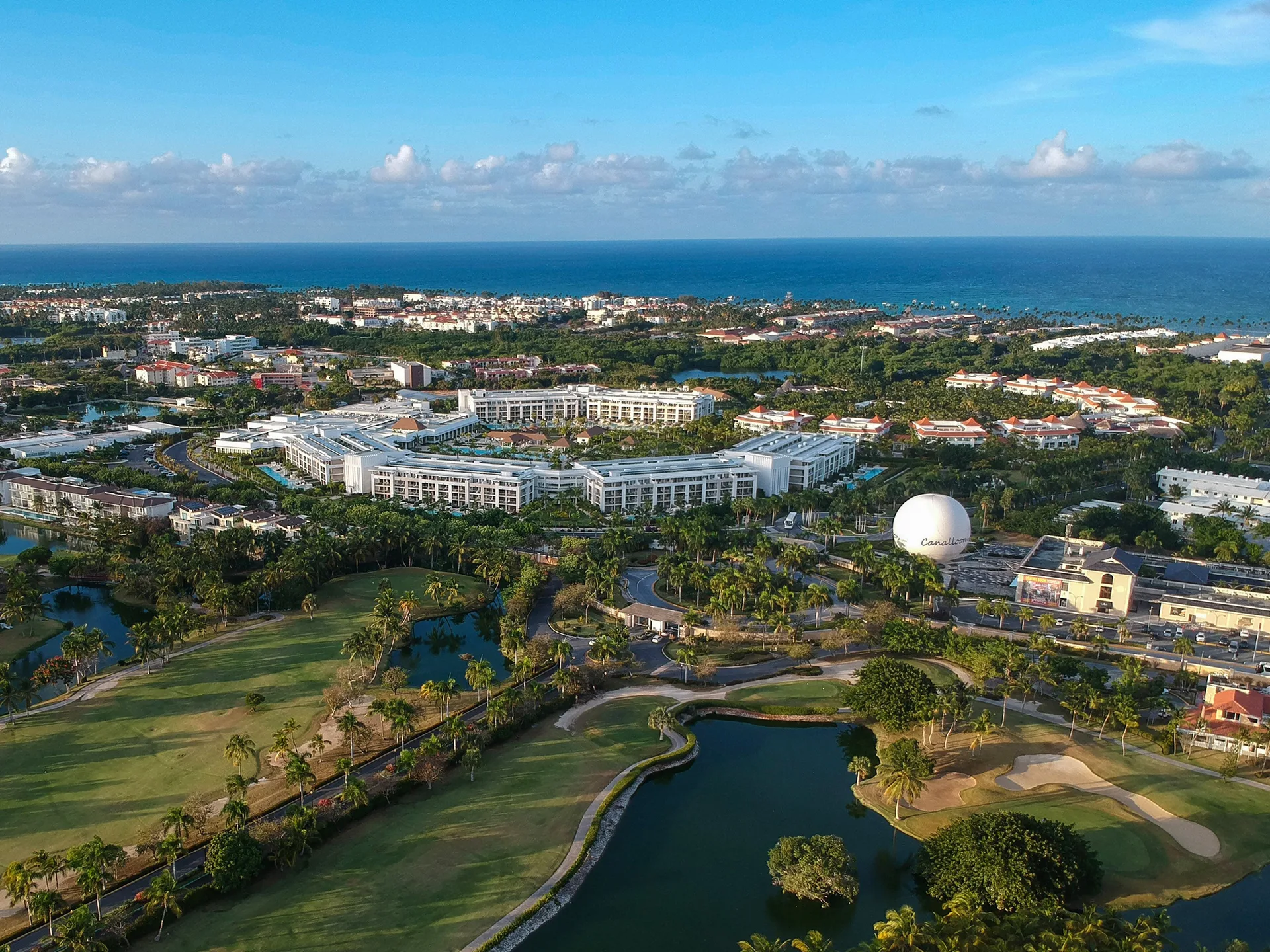 Aerial view of resort buildings, golf course lagoons, and ocean beyond Paradisus Grand Cana.