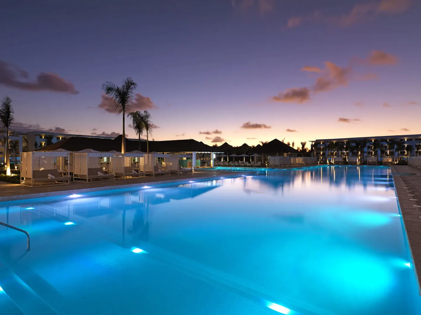Illuminated resort pool at dusk with cabanas at Paradisus Grand Cana.