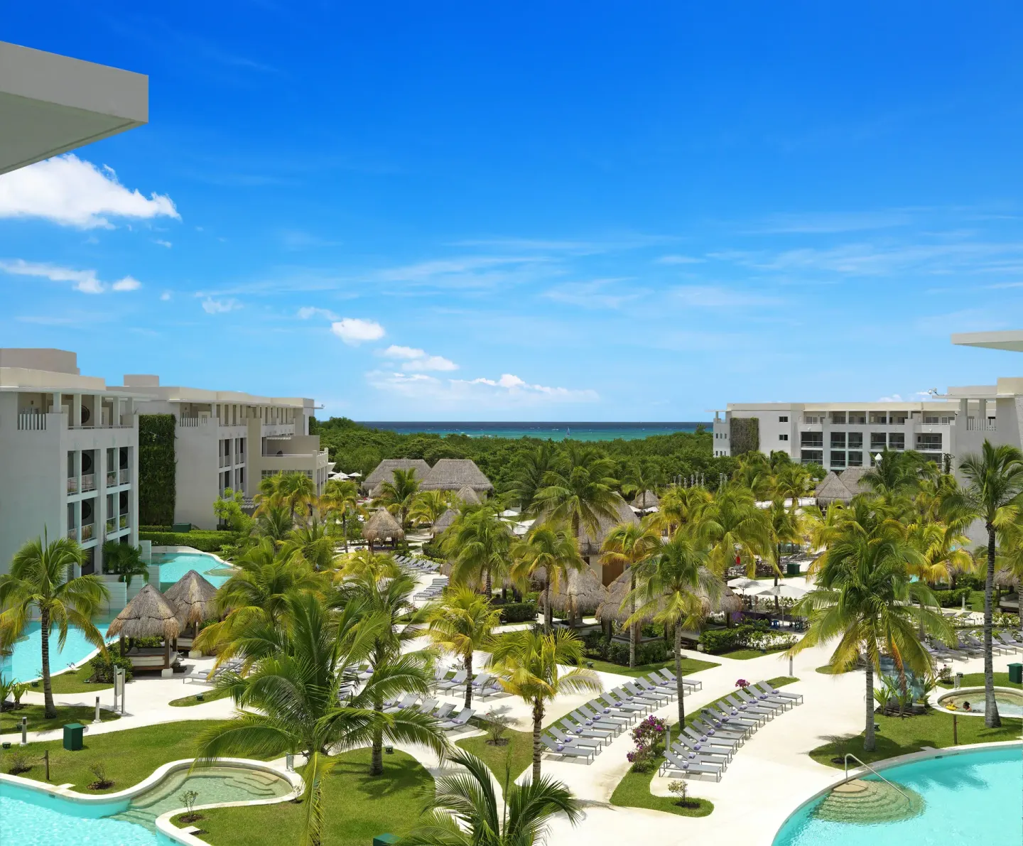Aerial view of pools, palms, loungers, and the sea at Paradisus La Perla Riviera Maya.