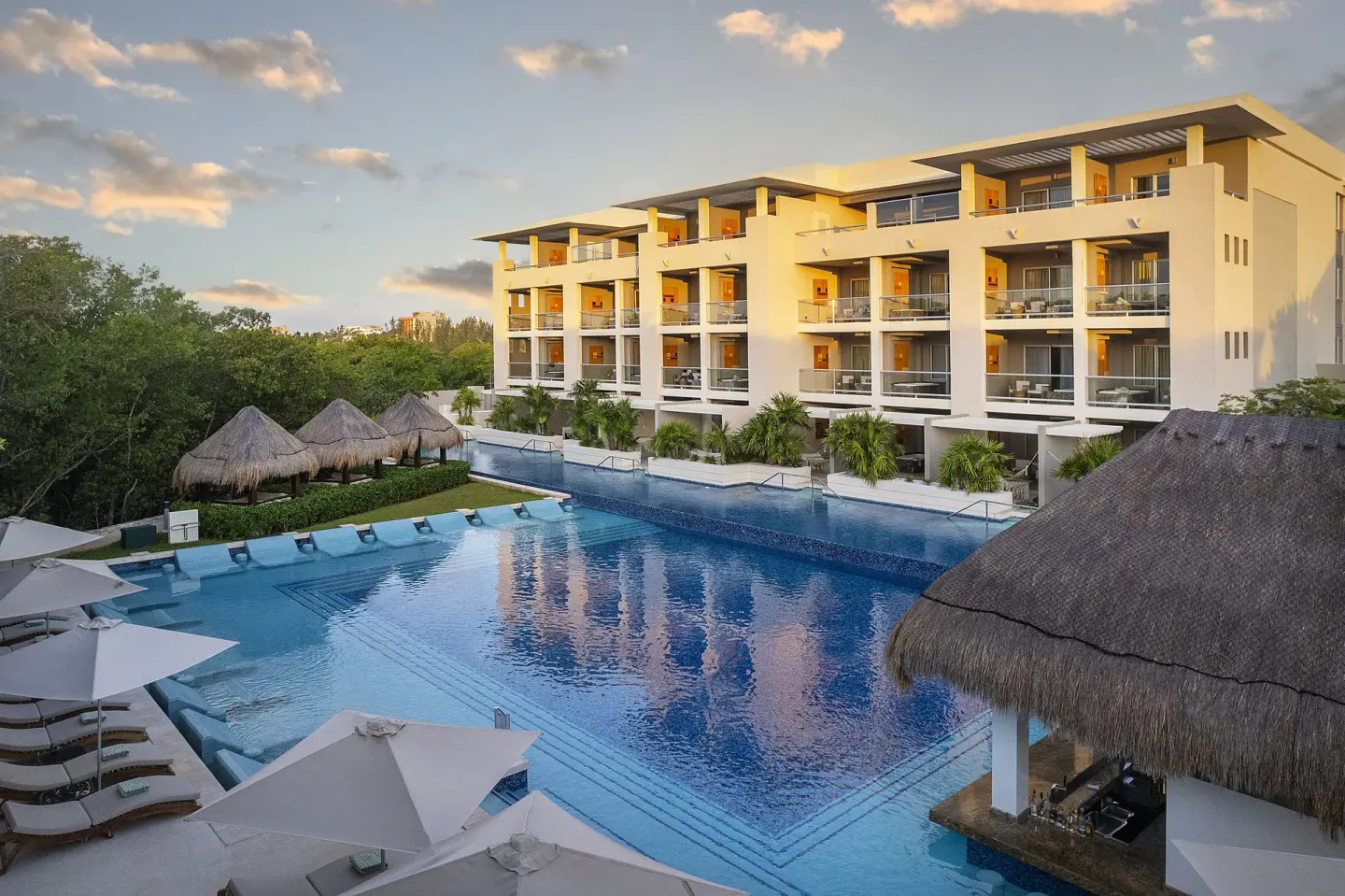Large pool and balcony-lined resort building at sunset at Paradisus La Perla Riviera Maya.