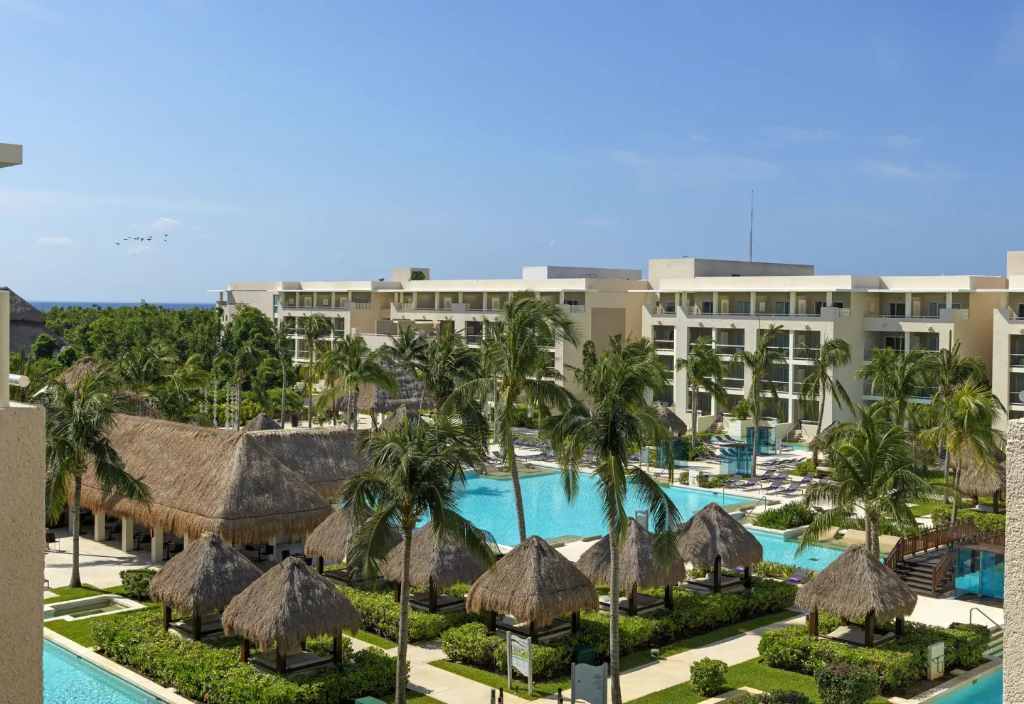 Thatched cabanas, palms, pool, and resort buildings at Paradisus La Perla Riviera Maya.