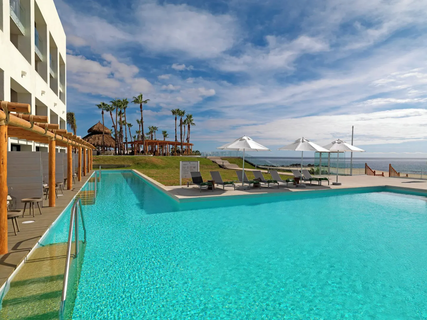 Oceanfront pool with loungers and white umbrellas at Paradisus Los Cabos.