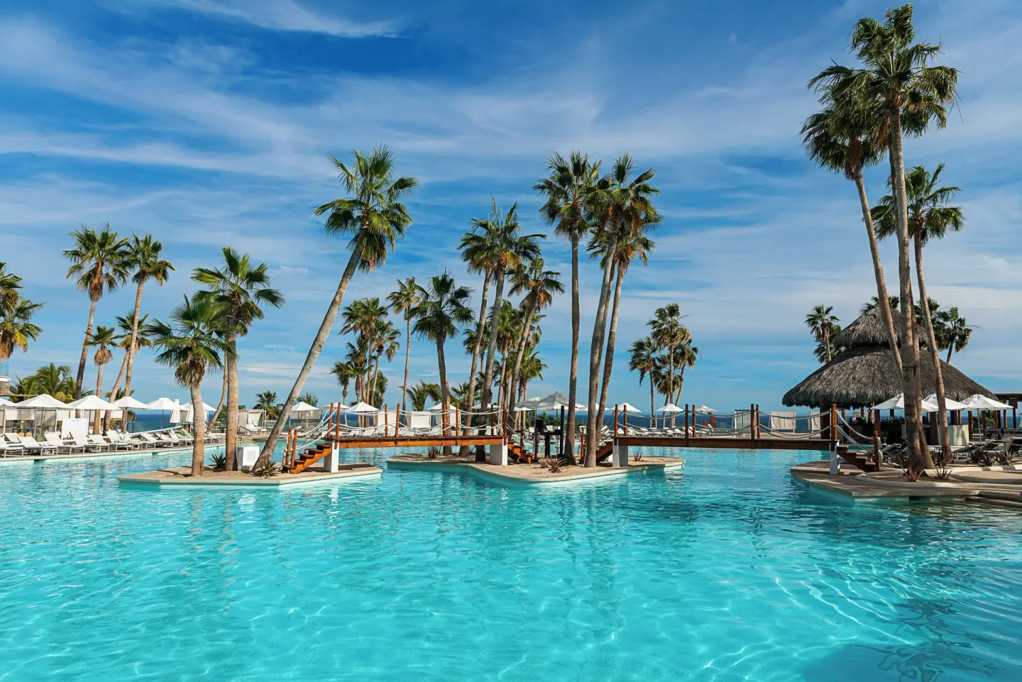 Resort pool with palm islands, bridges, and a palapa at Paradisus Los Cabos.