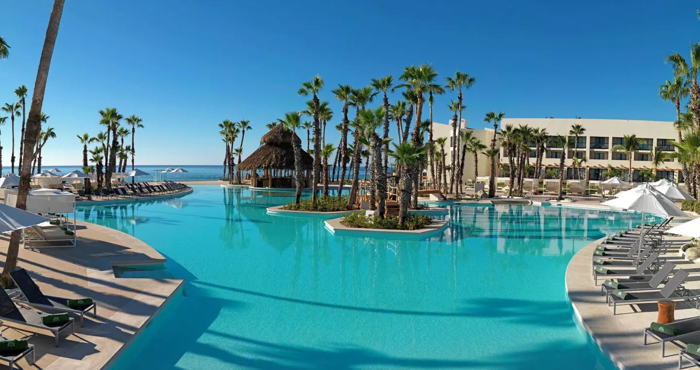 Large palm-lined resort pool with loungers at Paradisus Los Cabos.