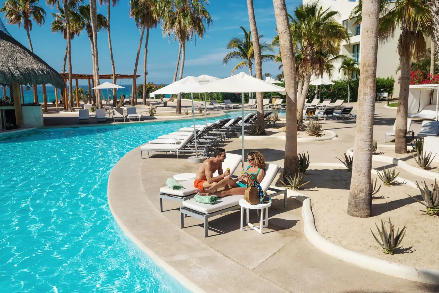 Couple lounges with drinks beside the palm-lined pool at Paradisus Los Cabos.