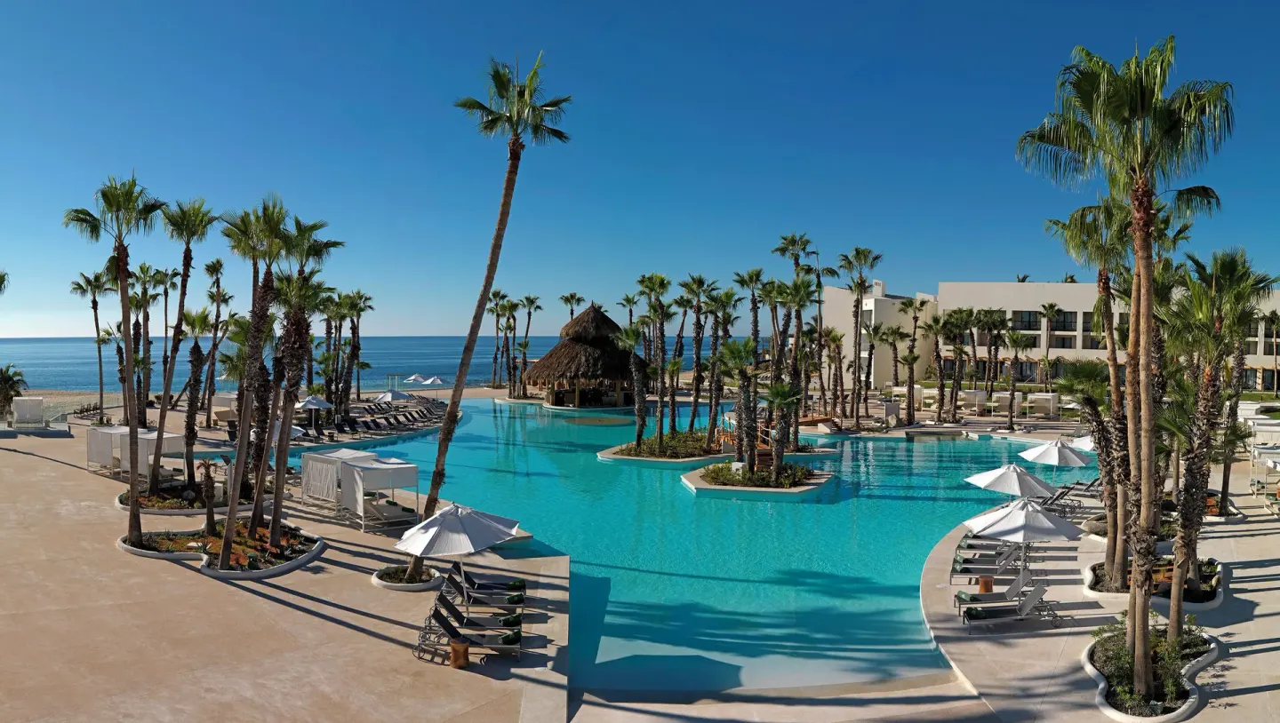 Wide resort pool with palm islands and ocean backdrop at Paradisus Los Cabos.