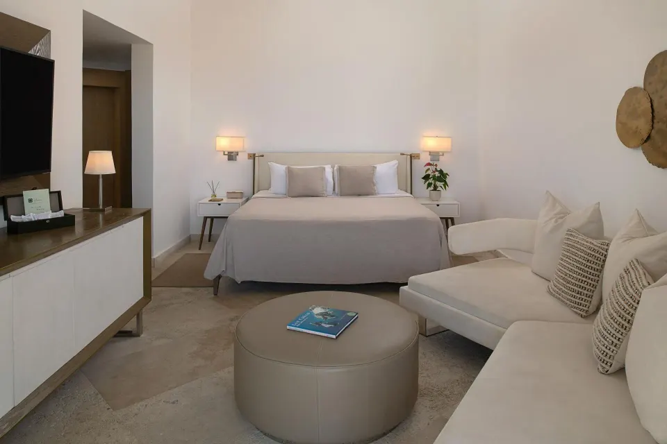 The Reserve Master Suite king bed at Paradisus Los Cabos with sofa seating, ottoman, and wall-mounted TV.