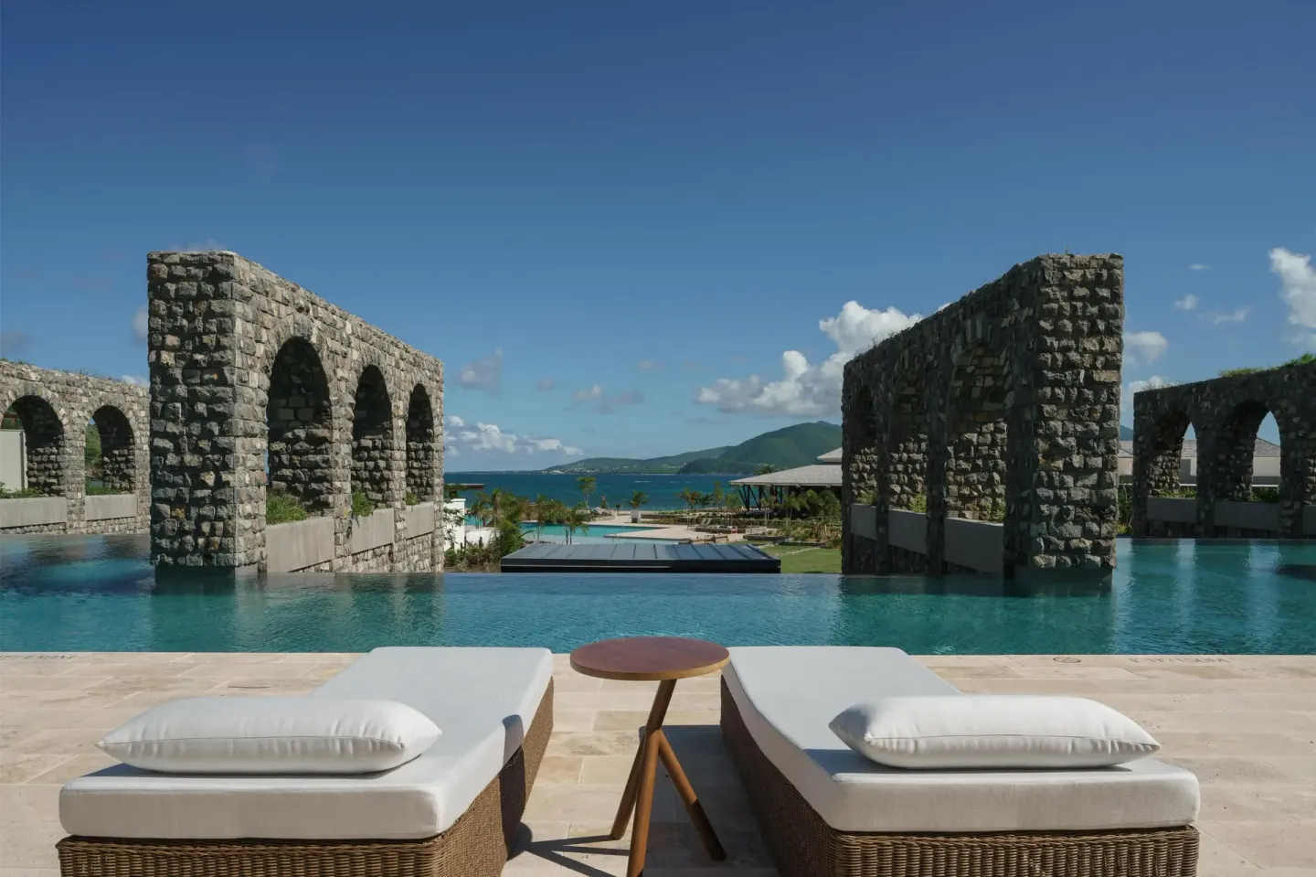 Cushioned loungers overlook a pool framed by stone arches at Park Hyatt St. Kitts.