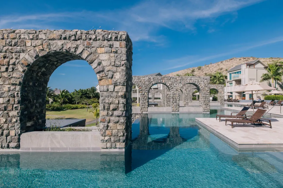 Pool with stone arch walls, lounge chairs, and resort buildings at Park Hyatt St. Kitts.