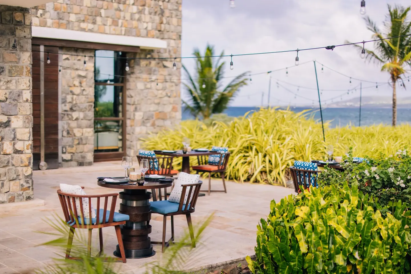 Outdoor stone-walled restaurant terrace with garden and sea glimpses at Park Hyatt St. Kitts.