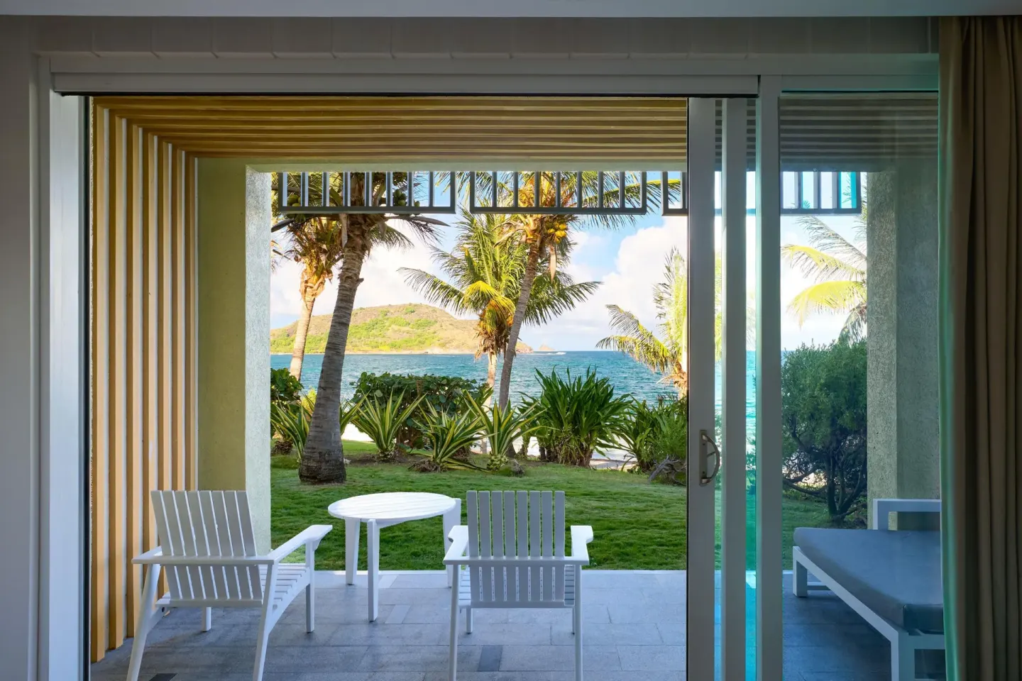 Beachfront room patio with chairs, lawn, palms and sea at Park Hyatt St. Kitts.