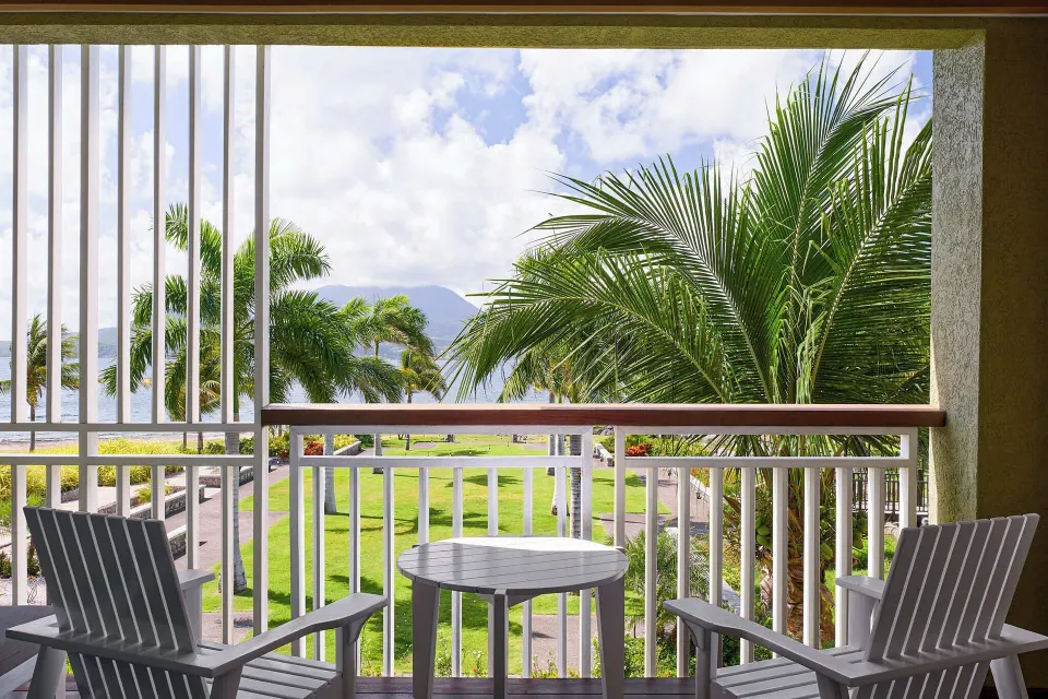 Guest room balcony with two chairs, table, palms, and sea view at Park Hyatt St. Kitts.