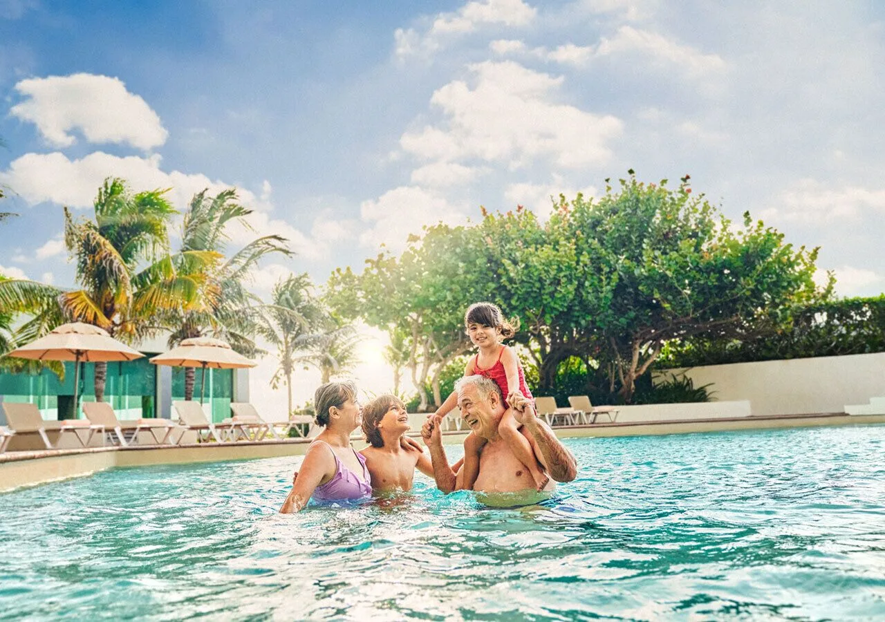 Family swimming in the pool at Park Royal Beach Cancun with palm trees and loungers behind them.