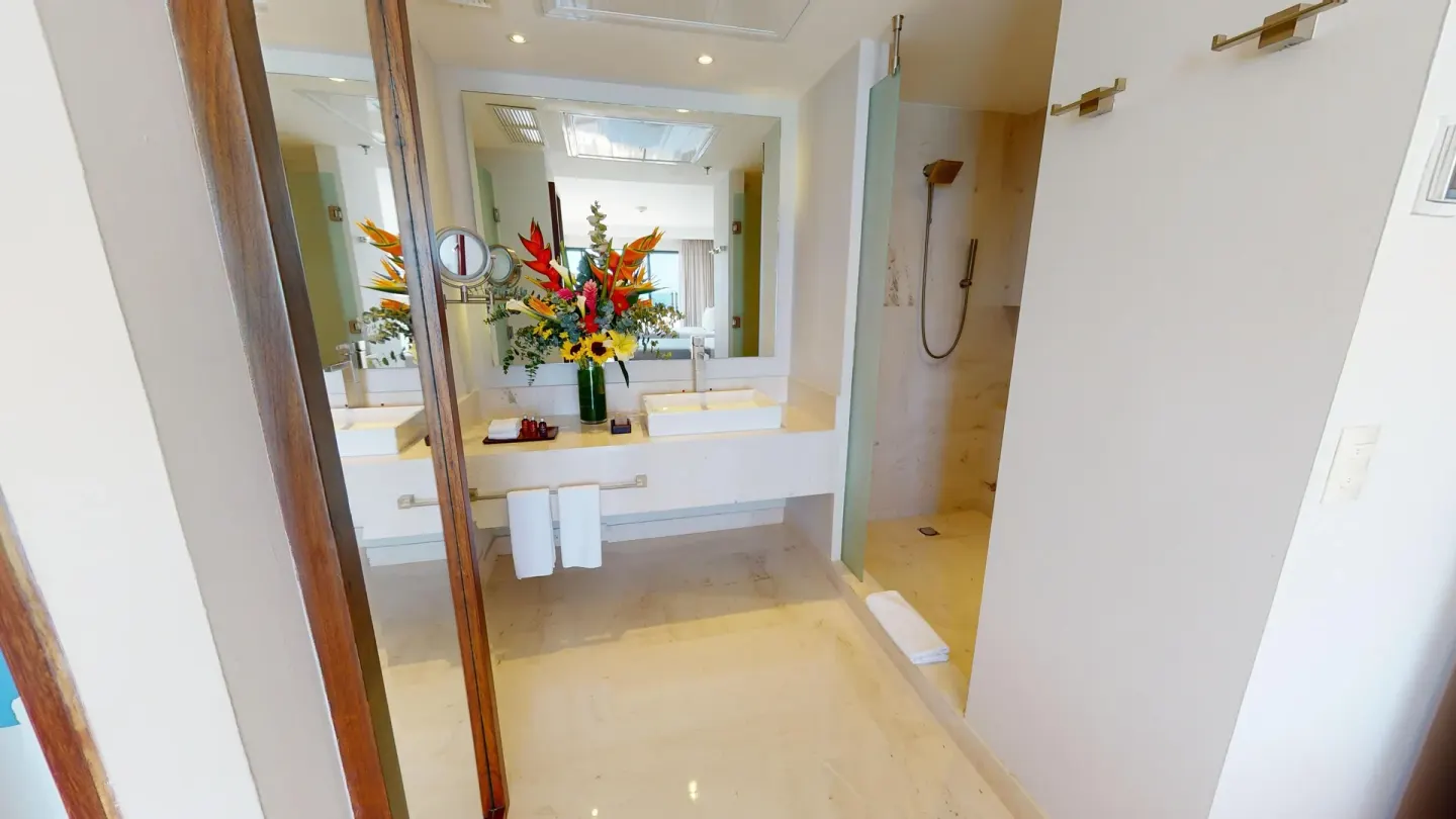 Guest bathroom vanity and shower at Park Royal Beach Cancun with flowers and towels.