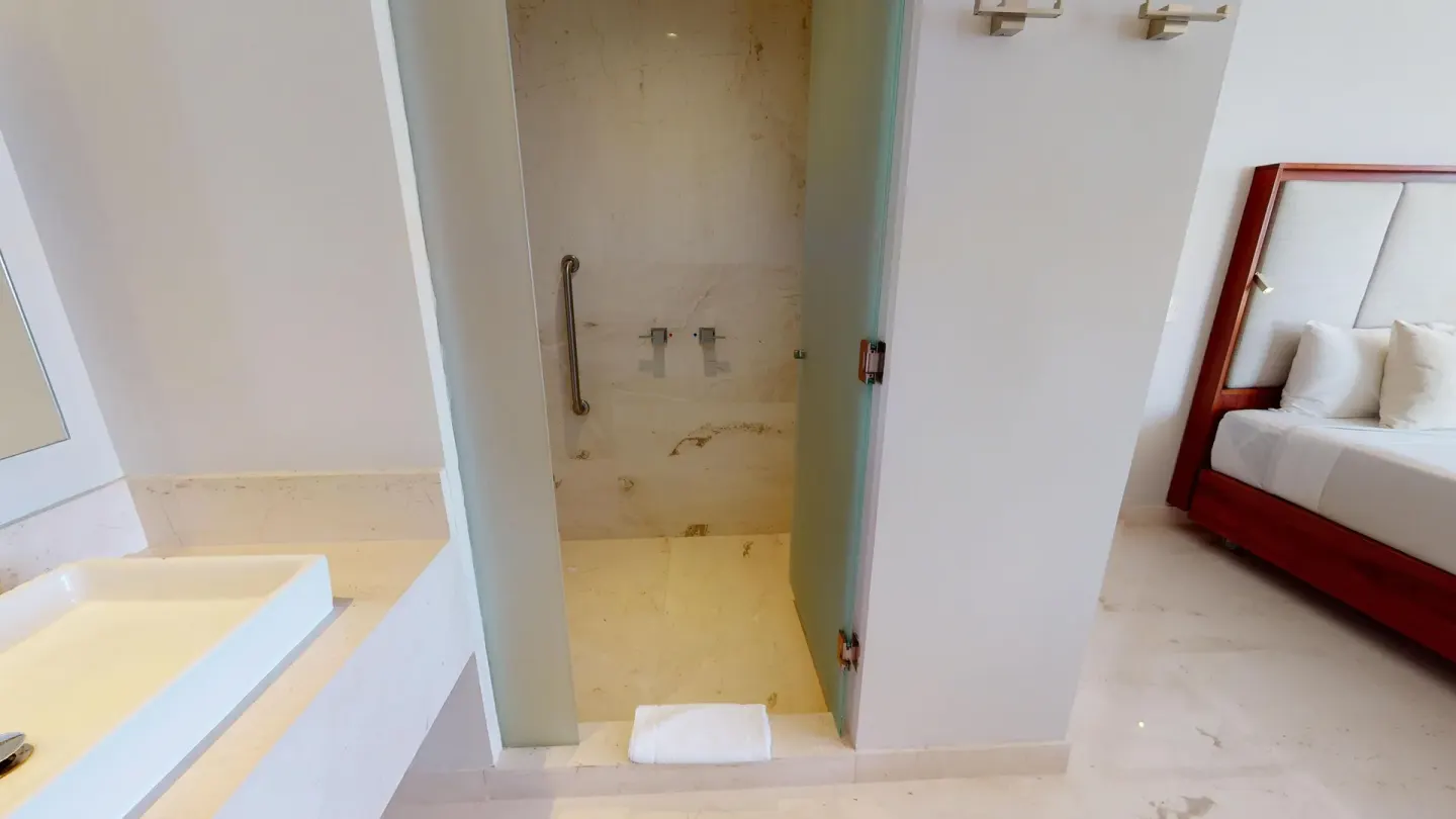 Walk-in shower beside a guest room bed at Park Royal Beach Cancun.