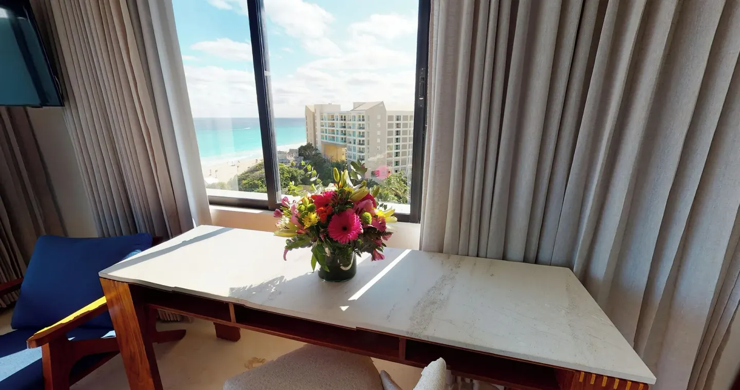 Guest room desk with flowers by an ocean-view window at Park Royal Beach Cancun.