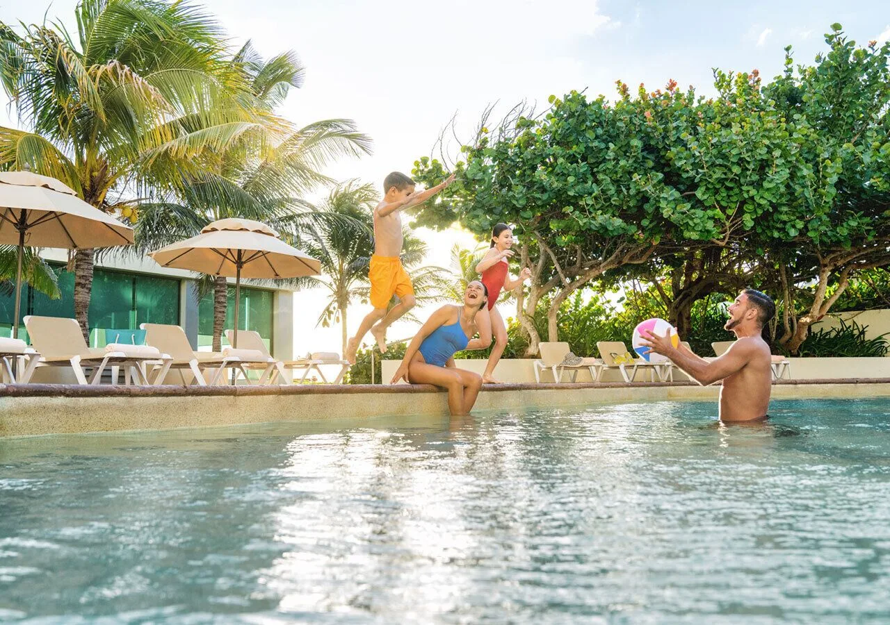 Guests playing in the pool near palms and loungers at Park Royal Beach Cancun.