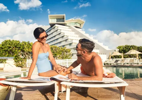 Couple relaxing on pool loungers with the hotel building at Park Royal Beach Cancun.